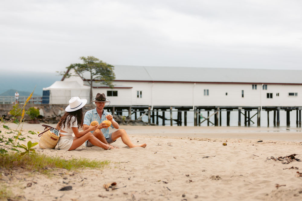 A couple enjoy coconut water on the beach next to the Sugar Wharf at Port Douglas. Douglas Shire Council has allocated $350,000 towards repairs of the iconic building and jetty in this year’s budget. Picture: Tourism Tropical North Queensland